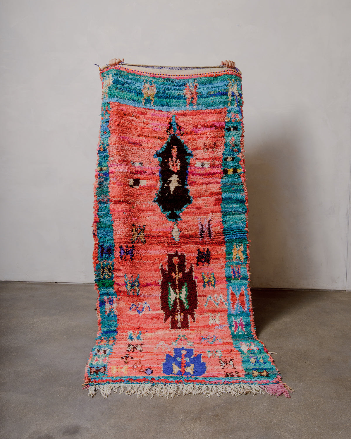 Berberlin vintage Boucherouite runner rug being held up against a white wall.